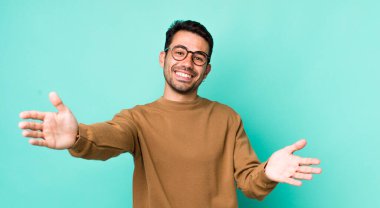 young handsome hicpanic man smiling cheerfully giving a warm, friendly, loving welcome hug, feeling happy and adorable