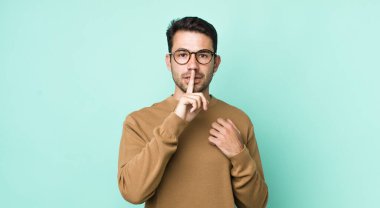 young handsome hicpanic man looking serious and cross with finger pressed to lips demanding silence or quiet, keeping a secret