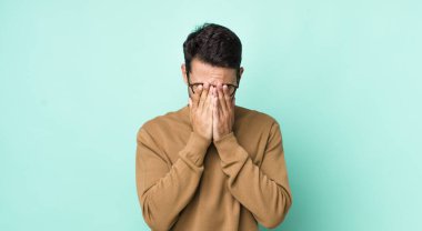 young handsome hicpanic man feeling sad, frustrated, nervous and depressed, covering face with both hands, crying