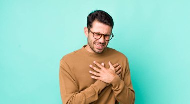 young handsome hicpanic man looking sad, hurt and heartbroken, holding both hands close to heart, crying and feeling depressed