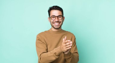 young handsome hicpanic man feeling happy and successful, smiling and clapping hands, saying congratulations with an applause