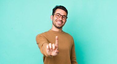 young handsome hicpanic man smiling proudly and confidently making number one pose triumphantly, feeling like a leader