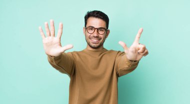 young handsome hicpanic man smiling and looking friendly, showing number seven or seventh with hand forward, counting down