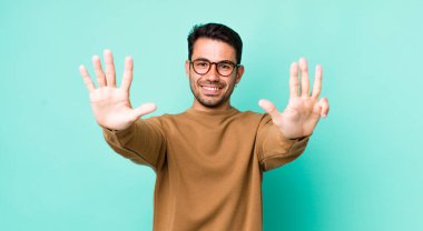 young handsome hicpanic man smiling and looking friendly, showing number nine or ninth with hand forward, counting down