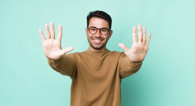 young handsome hicpanic man smiling and looking friendly, showing number ten or tenth with hand forward, counting down