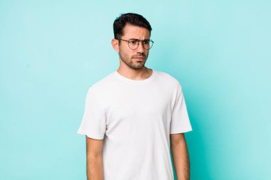 young handsome hicpanic man feeling sad, upset or angry and looking to the side with a negative attitude, frowning in disagreement