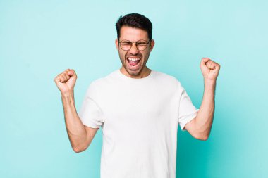 young handsome hicpanic man looking extremely happy and surprised, celebrating success, shouting and jumping