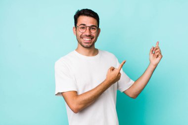 young handsome hicpanic man smiling happily and pointing to side and upwards with both hands showing object in copy space