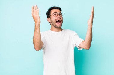 young handsome hicpanic man feeling happy, amazed, lucky and surprised, celebrating victory with both hands up in the air