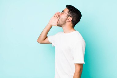 young handsome hicpanic man profile view, looking happy and excited, shouting and calling to copy space on the side