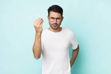 young handsome hicpanic man making capice or money gesture, telling you to pay your debts!