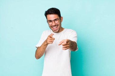 young handsome hicpanic man feeling happy, cool, satisfied, relaxed and successful, pointing at camera, choosing you