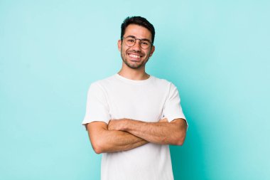 young handsome hicpanic man laughing happily with arms crossed, with a relaxed, positive and satisfied pose