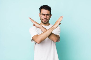 young handsome hicpanic man looking annoyed and sick of your attitude, saying enough! hands crossed up front, telling you to stop