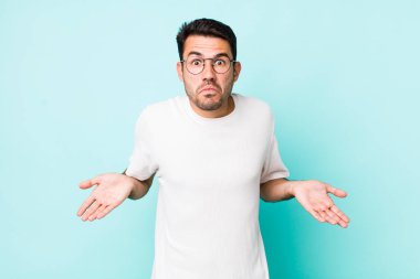 young handsome hicpanic man feeling clueless and confused, having no idea, absolutely puzzled with a dumb or foolish look