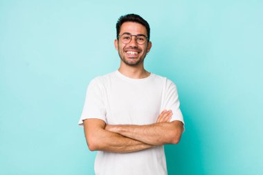 young handsome hicpanic man looking like a happy, proud and satisfied achiever smiling with arms crossed