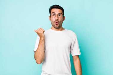 young handsome hicpanic man looking astonished in disbelief, pointing at object on the side and saying wow, unbelievable