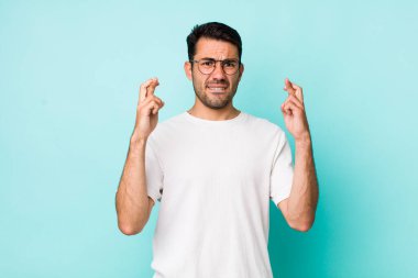 young handsome hicpanic man crossing fingers anxiously and hoping for good luck with a worried look