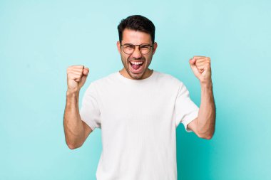 young handsome hicpanic man feeling happy, surprised and proud, shouting and celebrating success with a big smile