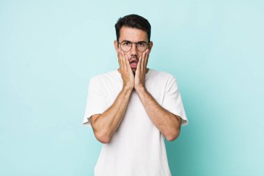 young handsome hicpanic man feeling shocked and scared, looking terrified with open mouth and hands on cheeks