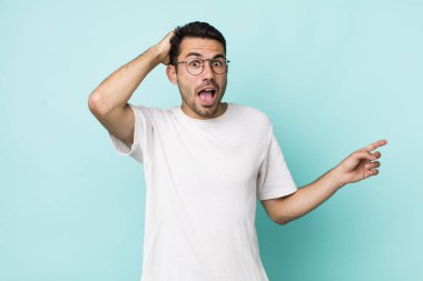 young handsome hicpanic man laughing, looking happy, positive and surprised, realizing a great idea pointing to lateral copy space