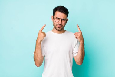 young handsome hicpanic man with a bad attitude looking proud and aggressive, pointing upwards or making fun sign with hands