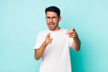 young handsome hicpanic man smiling with a positive, successful, happy attitude pointing to the camera, making gun sign with hands