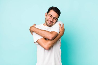 young handsome hicpanic man feeling in love, smiling, cuddling and hugging self, staying single, being selfish and egocentric