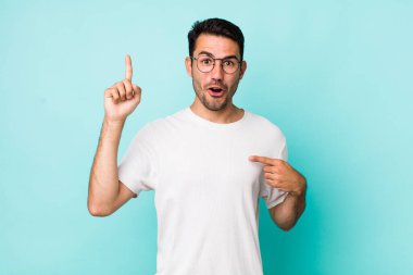 young handsome hicpanic man feeling proud and surprised, pointing to self confidently, feeling like successful number one