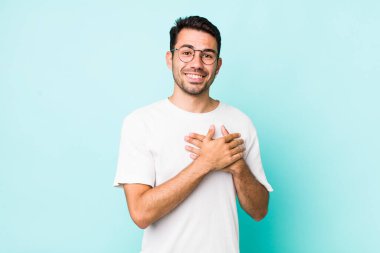 young handsome hicpanic man feeling romantic, happy and in love, smiling cheerfully and holding hands close to heart