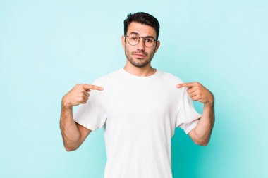 young handsome hicpanic man looking proud, positive and casual pointing to chest with both hands