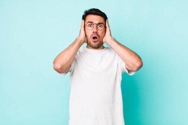 young handsome hicpanic man looking unpleasantly shocked, scared or worried, mouth wide open and covering both ears with hands