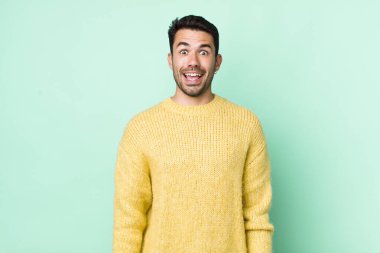 young handsome hicpanic man looking happy and pleasantly surprised, excited with a fascinated and shocked expression