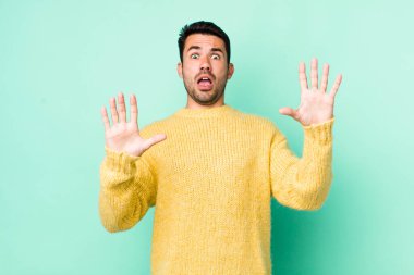 young handsome hicpanic man feeling stupefied and scared, fearing something frightening, with hands open up front saying stay away