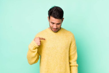 young handsome hicpanic man smiling cheerfully and casually, looking downwards and pointing to chest