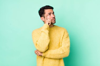 young handsome hicpanic man with a concentrated look, wondering with a doubtful expression, looking up and to the side