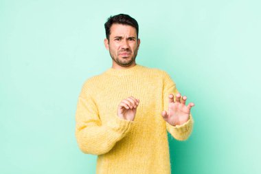 young handsome hicpanic man feeling disgusted and nauseous, backing away from something nasty, smelly or stinky, saying yuck