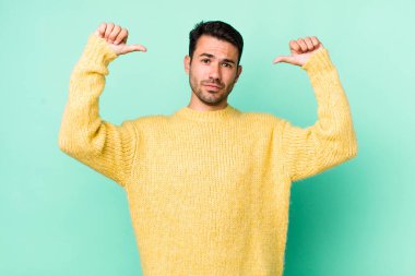 young handsome hicpanic man feeling proud, arrogant and confident, looking satisfied and successful, pointing to self