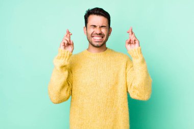 young handsome hicpanic man feeling nervous and hopeful, crossing fingers, praying and hoping for good luck