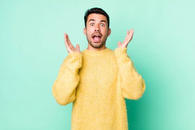 young handsome hicpanic man feeling shocked and excited, laughing, amazed and happy because of an unexpected surprise