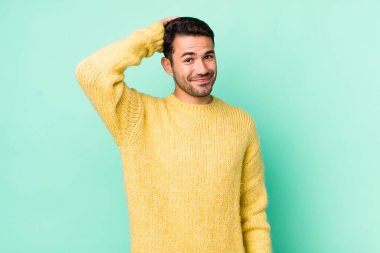 young handsome hicpanic man smiling cheerfully and casually, taking hand to head with a positive, happy and confident look