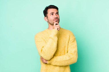 young handsome hicpanic man thinking, feeling doubtful and confused, with different options, wondering which decision to make