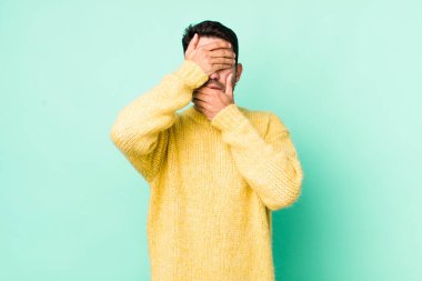 young handsome hicpanic man covering face with both hands saying no to the camera! refusing pictures or forbidding photos