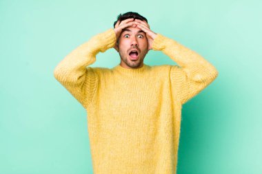 young handsome hicpanic man feeling horrified and shocked, raising hands to head and panicking at a mistake