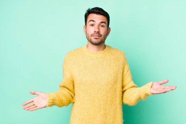 young handsome hicpanic man feeling puzzled and confused, unsure about the correct answer or decision, trying to make a choice