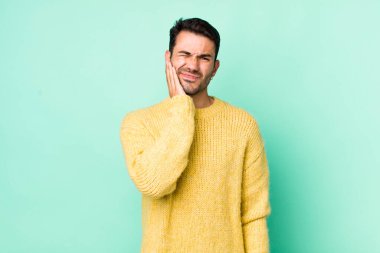 young handsome hicpanic man holding cheek and suffering painful toothache, feeling ill, miserable and unhappy, looking for a dentist
