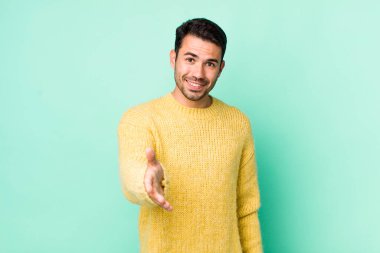 young handsome hicpanic man smiling, looking happy, confident and friendly, offering a handshake to close a deal, cooperating