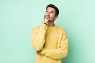 young handsome hicpanic man feeling thoughtful, wondering or imagining ideas, daydreaming and looking up to copy space