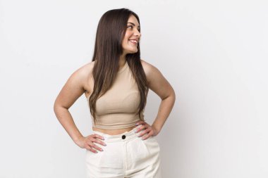 Genç, güzel bir kadın mutlu, neşeli ve kendinden emin görünüyor. Gururla gülümsüyor ve iki elini de kalçasında istiyor.