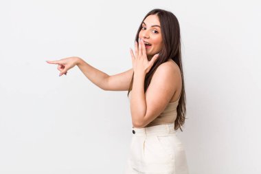Genç, güzel bir kadın kendini mutlu, şok olmuş ve şaşırmış hissediyor. Ağzını eliyle kapatıyor ve yanal kopya alanını işaret ediyor.